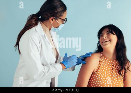 Smiling woman getting vaccinated. Doctor wearing face mask and protective gloves giving vaccine injection a happy female patient. Stock Photo