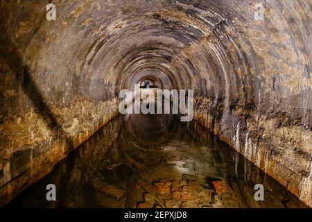 Flooded vaulted sewer tunnel with water reflection. Stock Photo