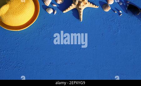 Frame with beach accessories on a nautical theme: yellow straw hat, sunglasses, starfish and shells on a blue background. Vacation concept, sea trip, Stock Photo