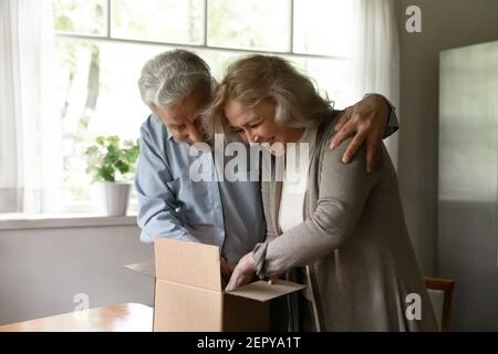 Happy excited mature family couple unpacking parcel at home Stock Photo