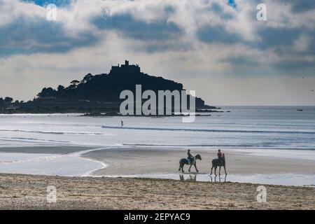 Marazion, Cornwall, UK. 28th February 2021. UK Weather. Horse riders and a distant paddleboarder on the beach at Marazion today, in the warm sunshine ahead of the start of spring on Monday. Credit Simon Maycock / Alamy Live News. Stock Photo