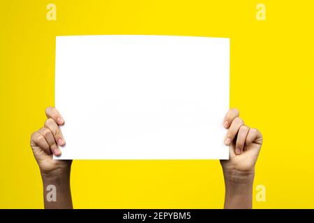 Hands holding blank white paper board poster placard on yellow background Stock Photo