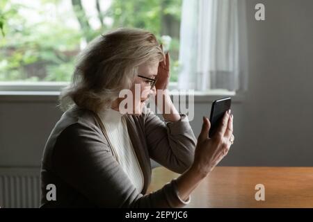 Confused senior 60s woman holding head, feeling dizziness Stock Photo