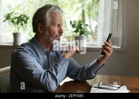 Serious mature smartphone user reading message on screen Stock Photo