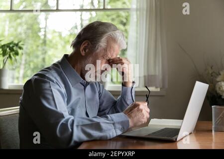 Tired mature 60s man working at laptop from home Stock Photo