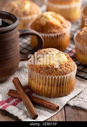 Cinnamon muffin next to coffee mug with muffins on a wire rack in background