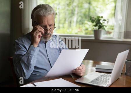 Focused mature man reading financial document or received paper Stock Photo