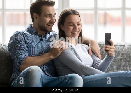 Happy millennial husband and wife using mobile phone Stock Photo