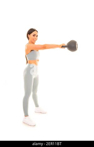 Vertical portrait of a young woman lifting a 15kg kettlebell whilst doing a workout, isolated on a white background. Stock Photo