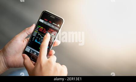 Close-up hand holding mobile phone with analyzing graph and the trending chart with stock set market application that everywhere can be trading. Stock Photo