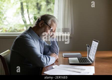 Focused pensive senior man working from home, using laptop Stock Photo
