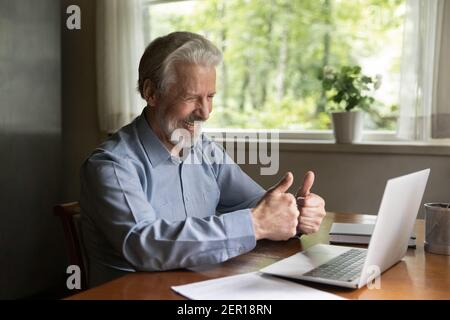 Happy grey haired senior man using laptop for video call Stock Photo