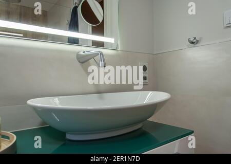 Detail of a vanity unit. Sink mounted on a cabinet, with a wall tap. The cabinet is covered with a striking green glass plate. The faucet is mounted o Stock Photo