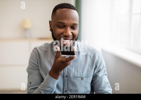 African Man Using Voice Search Holding Smartphone Near Mouth Indoor Stock Photo