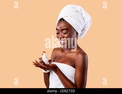 Smiling Black Woman In Towel Pouring Body Lotion On Palm Stock Photo