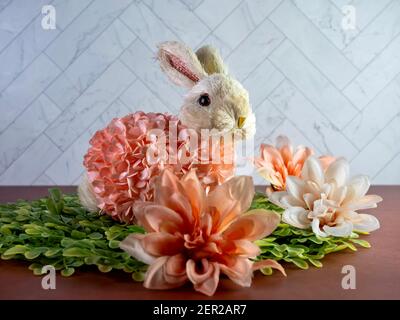 Easter Bunny Decor sitting on green leaves surrounded by peach artificial dahlia flower  blooms, perfect for the spring holiday! Stock Photo