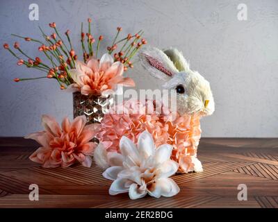 Easter Bunny Decor sitting on a wooden surface surrounded by peach artificial dahlia flower  blooms, perfect for the spring holiday! Stock Photo