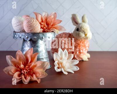 Easter Bunny Decor sitting by a Raised Rustic Metal Dish Filled with String Decorated Easter Eggs surrounded by peach artificial dahlia flower  blooms Stock Photo