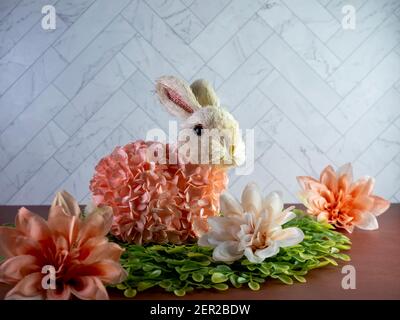 Easter Bunny Decor sitting on green leaves surrounded by peach artificial dahlia flower  blooms, perfect for the spring holiday! Stock Photo