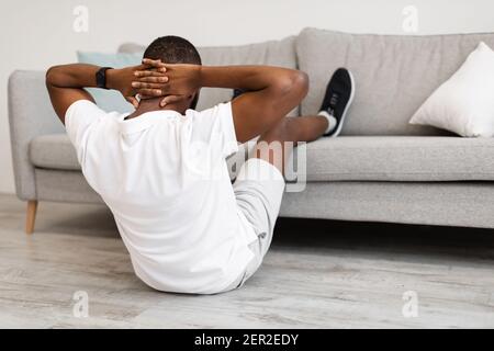 Guy Doing Abs With Legs On Sofa Exercising Indoor, Back-View Stock Photo