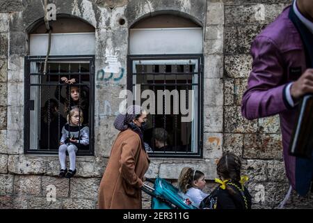 Jerusalem, Israel. 28th Feb, 2021. Ultra orthodox Jewish children look out from windows to watch the celebrations of the Jewish holiday of Purim at Jerusalem's Mea She'arim neighbourhood. Purim, also called the Festival of Lots, is a carnival-like Jewish holiday that commemorates the saving of the Jewish people from a plot to massacre all the Jews in the ancient Persian Empire, as recounted in the Book of Esther. Credit: Ilia Yefimovich/dpa/Alamy Live News Stock Photo