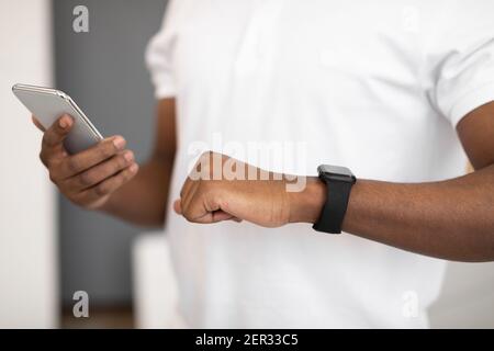 Unrecognizable Black Man Using Workout Gadgets Smartphone And Smartwatch Indoors Stock Photo