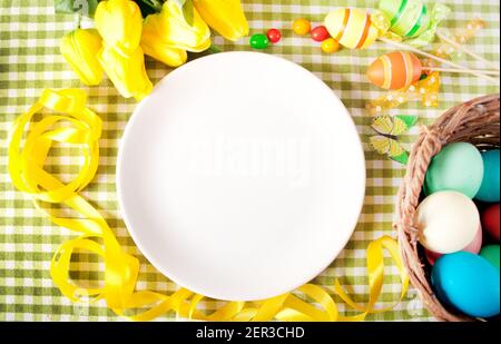 Easter table setting with white plate, basket of colorful eggs, candles and yellow tulips Stock Photo