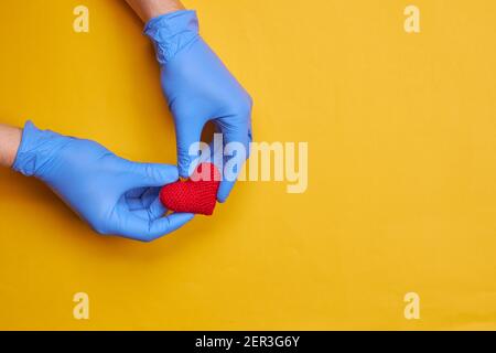 red heart symbol at persons hand with blue medical gloves on. yellow or orange background with copy space. heart disease concept Stock Photo