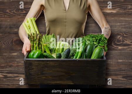 Unrecognizable wooman holds in hands wooden box with various fresh green vegetables Stock Photo