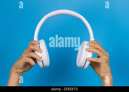 Hands holding modern white wireless headphones on light blue background Stock Photo