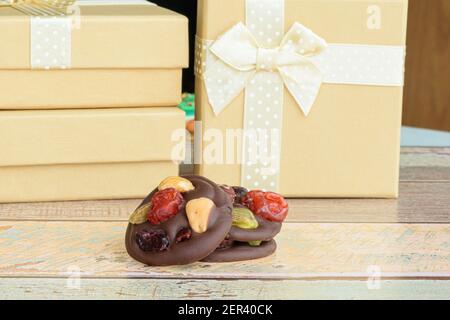 Three chocolate chip cookies with nuts. Small golden gift boxes in the background. Stock Photo