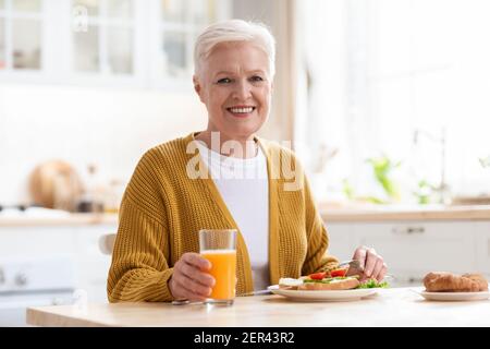 Attractive grandmother having lunch in kitchen alone Stock Photo