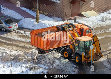 Winter snow removal from sidewalks. A mini tractor shovels snow and loads it into the back of a truck. View from above. Stock Photo