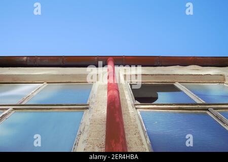 Old red rain pipe on a white building with windows in fron of a blue sky Stock Photo