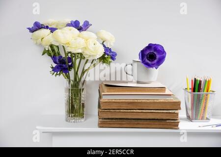 One blue anemone in a cup in the style of the seventies on the table with books as an interior decoration. Pencil holders with pencils. Bouquet of whi Stock Photo