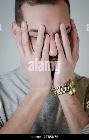 Portrait of a young man with a short beard who covers his face with his hands in a moment of sadness Stock Photo