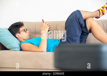 Arabic boy lying down on sofa and playing with smart phone Stock Photo