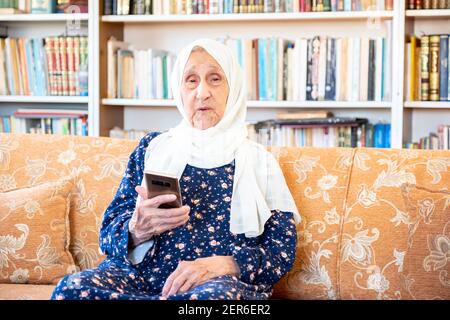 Happy old arabic muslim woamn using technology while sitting on couch Stock Photo