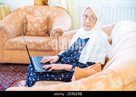 Happy old arabic muslim woamn using technology while sitting on couch Stock Photo