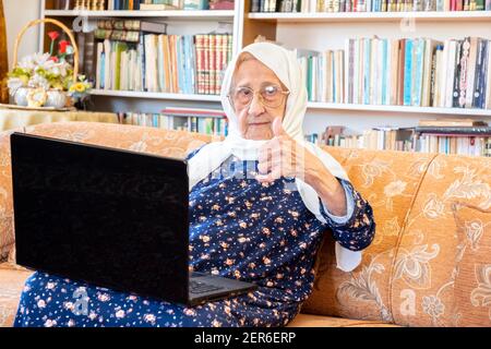 Happy old arabic muslim woamn using technology while sitting on couch Stock Photo