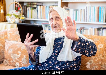 Happy old arabic muslim woamn using technology while sitting on couch Stock Photo