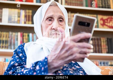 Happy old arabic muslim woamn using technology while sitting on couch Stock Photo