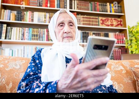 Happy old arabic muslim woamn using technology while sitting on couch Stock Photo