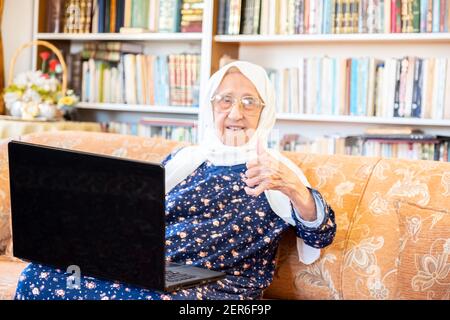 Happy old arabic muslim woamn using technology while sitting on couch Stock Photo