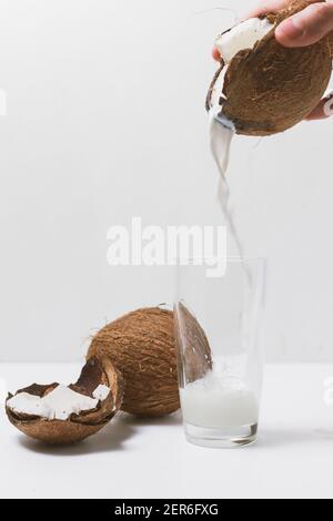 Man's hand pours coconut milk into glass from cracked coconut Stock Photo