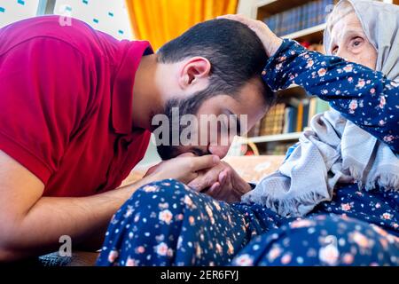 Arabic muslim guy kissing his grand mother hand out of respect Stock Photo