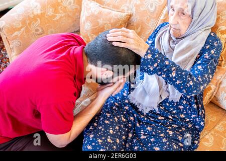 Arabic muslim guy kissing his grand mother hand out of respect Stock Photo