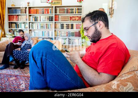 Arabic muslim guy sitting on couch surfing internet using his mobile Stock Photo