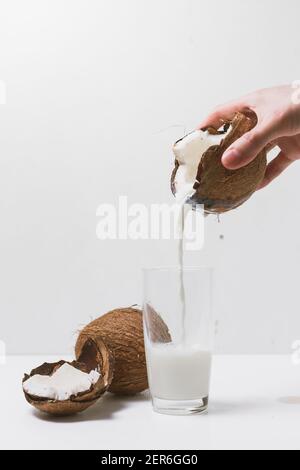 Man's hand pours coconut milk into glass from cracked coconut Stock Photo