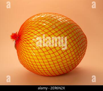 Mature pomelo in a net on a peach background Stock Photo